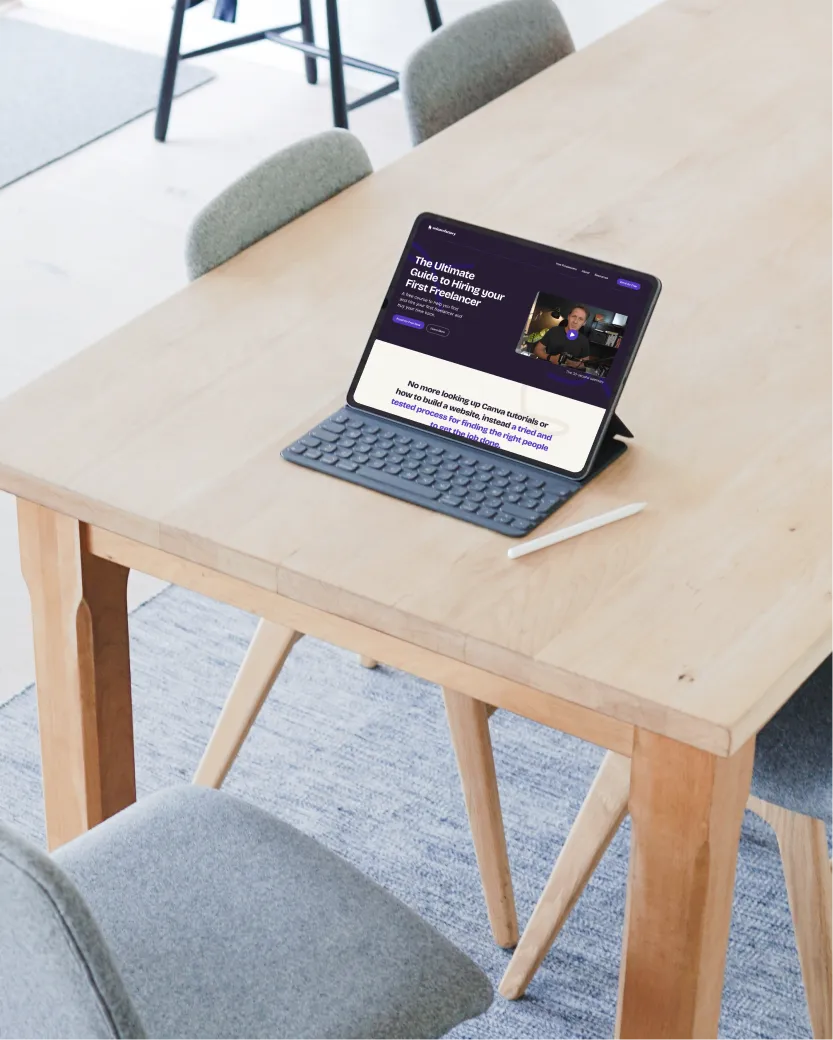 Tablet with keyboard and stylus on a wooden table displaying 'The Ultimate Guide to Hiring your First Freelancer' webpage.